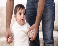 Baby walking with adult holding their arms for support