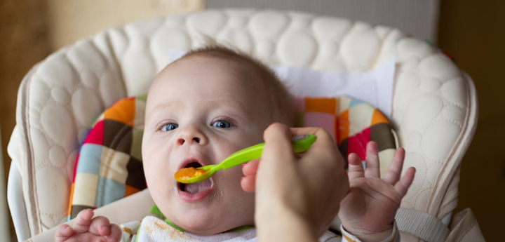 Baby boy sitting in a highchair being fed food from a spoon