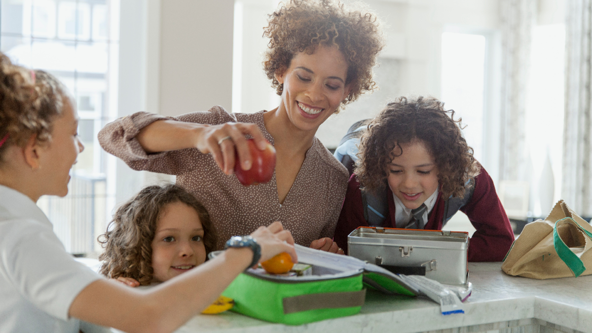 woman helping 3 children pack their lunches