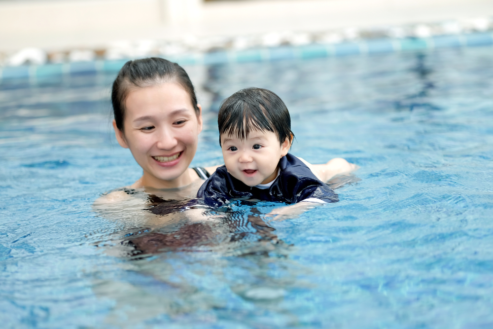 A mum holding her baby in a swimming pool, teaching them how to swim.