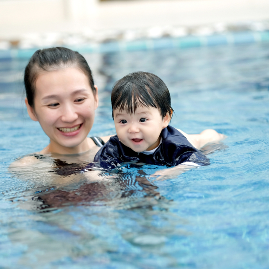 A mum holding her baby in a swimming pool, teaching them how to swim.