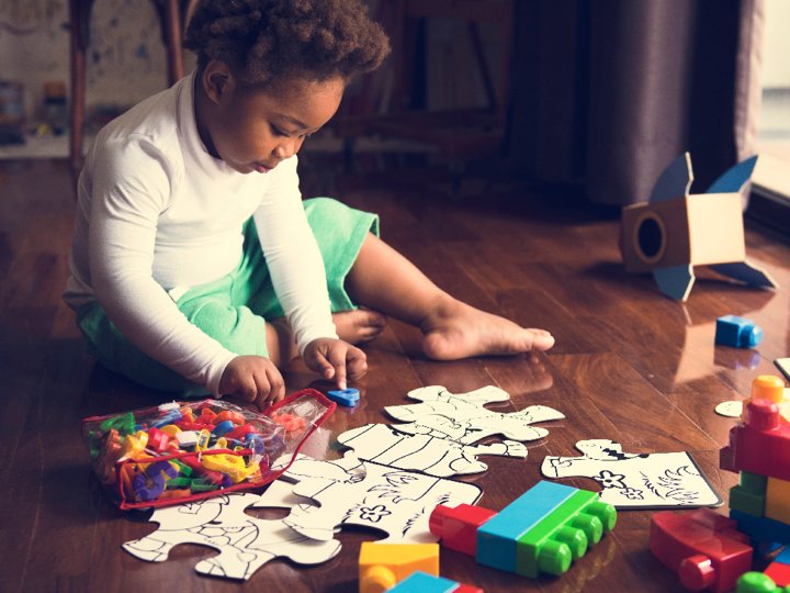 Child sitting on the floor playing with puzzle pieces, Duplo blocks and magnetic plastic letters