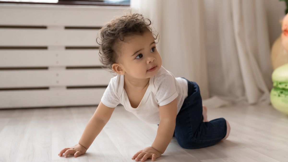 Baby crawling on their hands and knees across the floor.