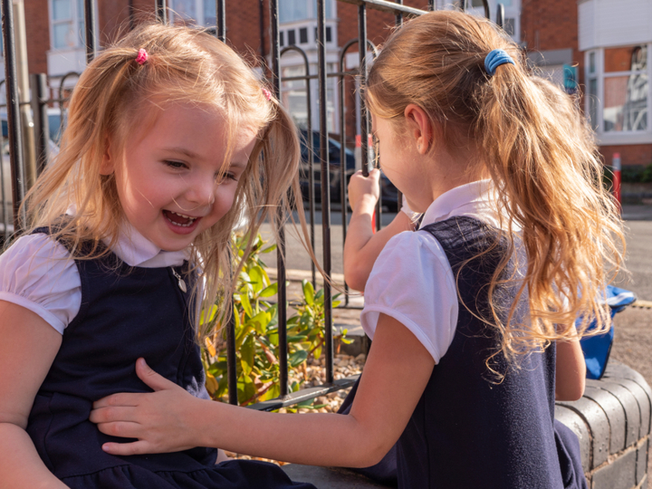 Two young primary school girls laughing together in the playground.