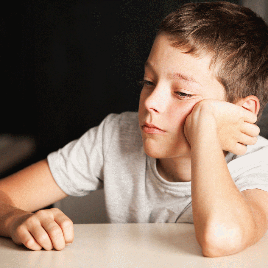 boy sat at table with head resting against hand looking bored