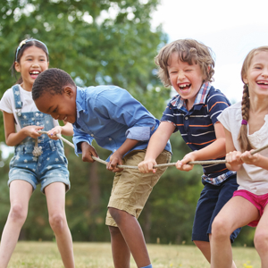 Four children pulling a rope in a game of tug of war whilst laughing and smiling outside in a park.