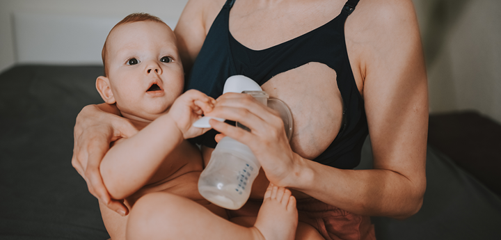 Expressing milk with hand pump, baby in other arm