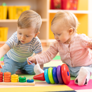 2 children playing with wooden stacking toys on the floor