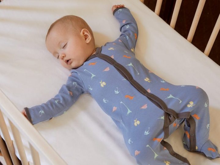 Baby lying in a cot with their arms stretched out