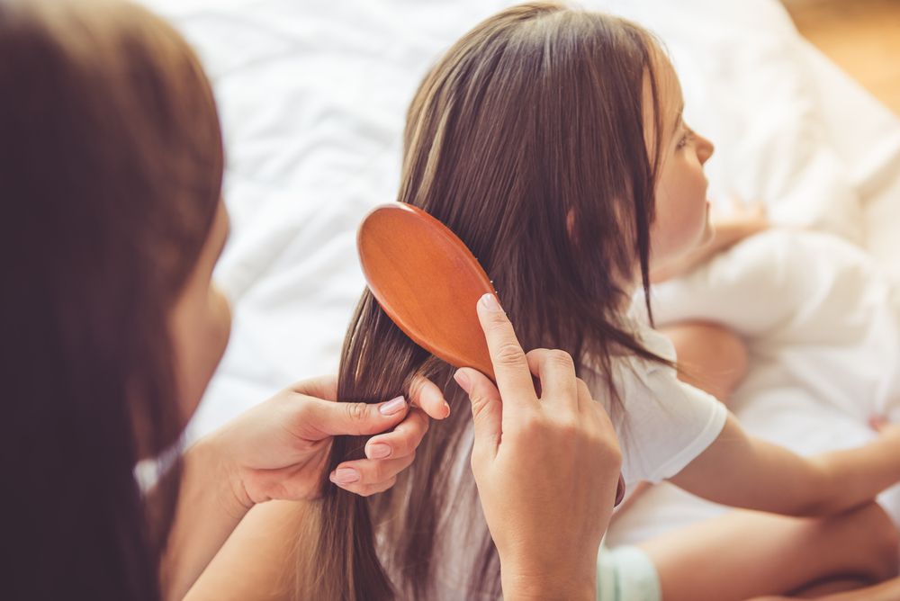 Young girl sitting on a bed having her hair brushed by her mum.