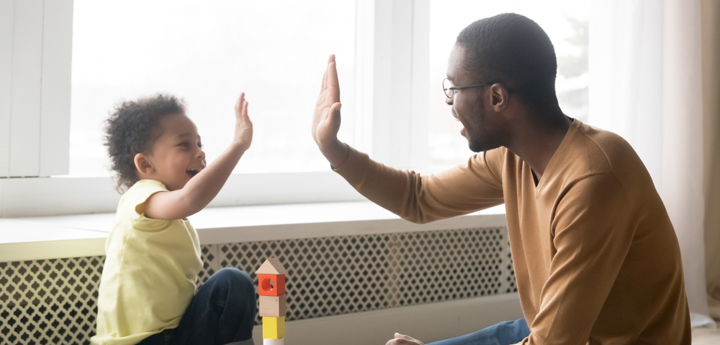 Young child and adult high-fiving whilst sitting on the floor.