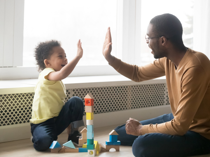 Young child and adult high-fiving whilst sitting on the floor.