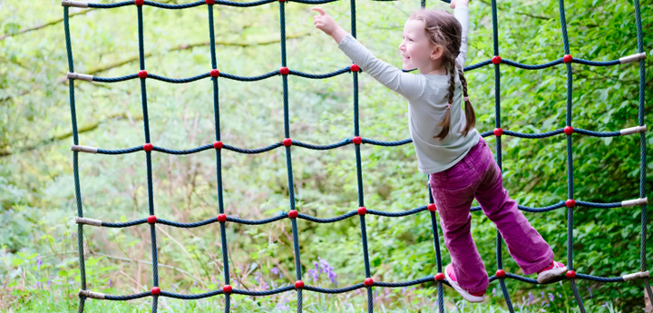 Young girl climbing on a rope net climbing frame in a woodland adventure playground. 