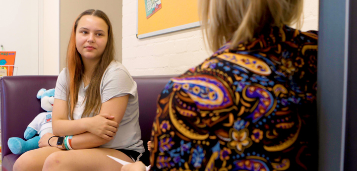 Young woman sat with arms crossed, speaking to a woman in the foreground