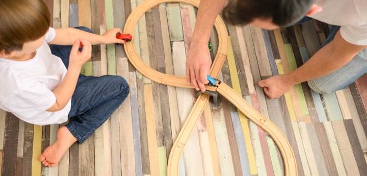 Man and young boy playing with toy cars on a wooden car track