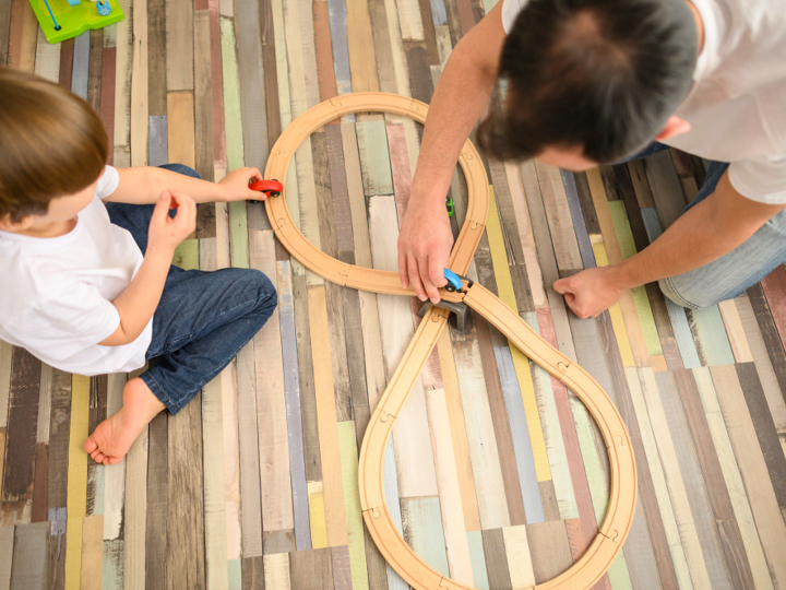 Man and young boy playing with toy cars on a wooden car track