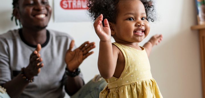 Toddler taking first steps with smiling adult in background