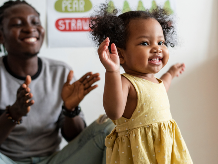 Toddler taking first steps with smiling adult in background