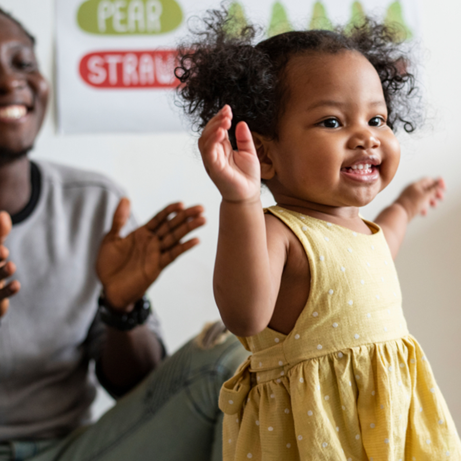 Toddler taking first steps with smiling adult in background