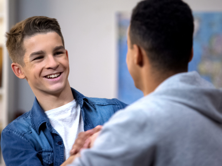 Two teenage boys smiling at one another and handshaking.