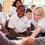 Children In A Class Looking At A Book Held By A Teacher