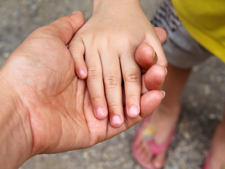 An adults hand is outstretched and a small child has placed their hand in the adults
