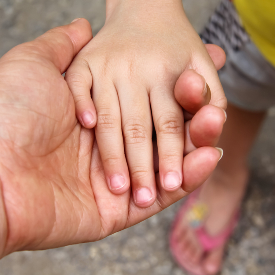 An adults hand is outstretched and a small child has placed their hand in the adults