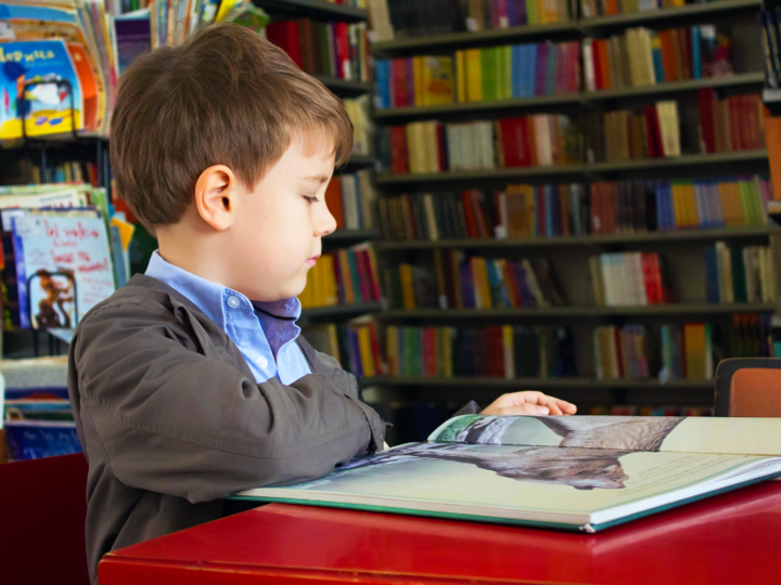 Young boy sitting at a table in a library reading a book