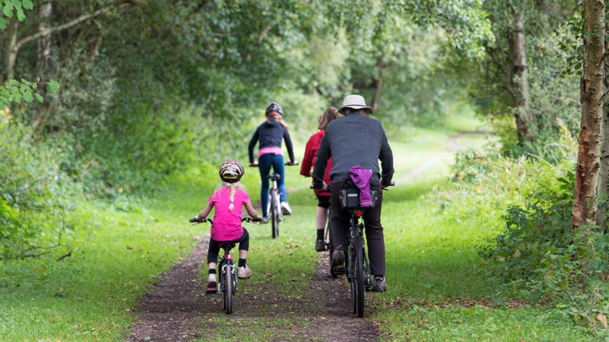 Family cycling down a grass track through a woodland area.