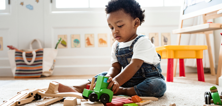 Toddler sitting on the floor in a playroom playing with wooden toys 