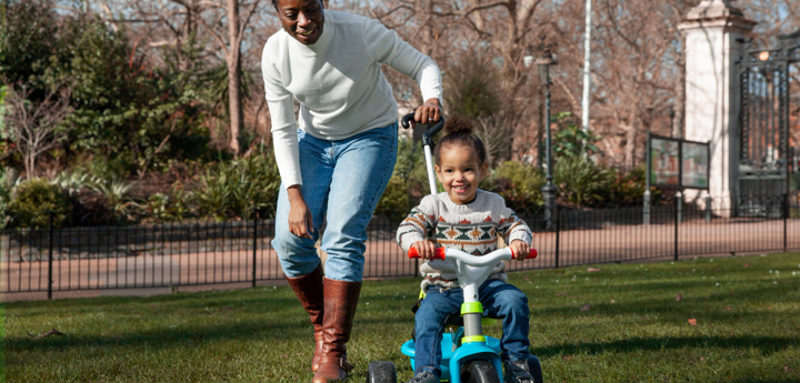Mother pushing child through park on tricycle