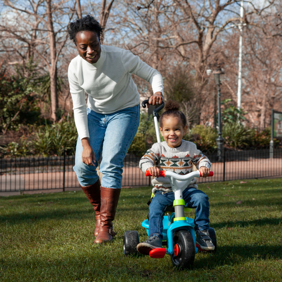 Mother pushing child through park on tricycle