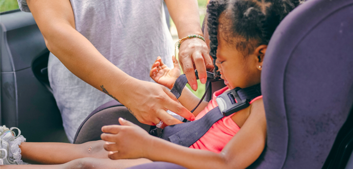 Child being clipped into a car seat by an adult