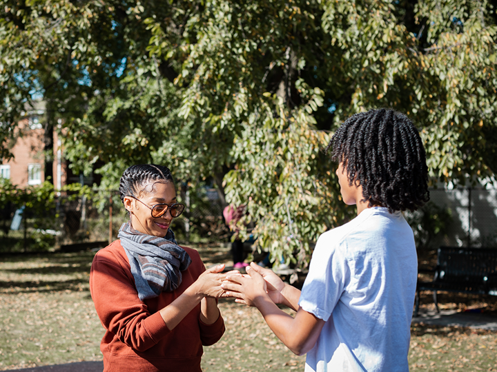 adult woman and teenage boy playing hand slap game outdoors