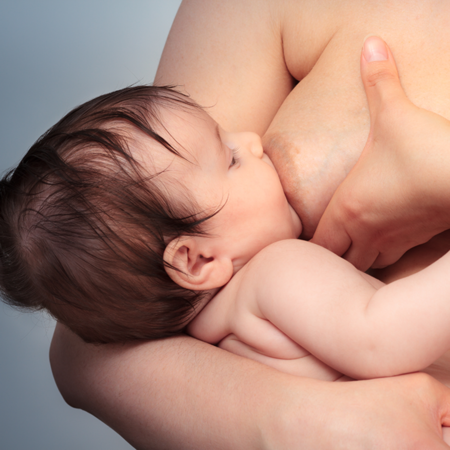 Breastfeeding baby with dark hair. Breastfeeding parent holding breast