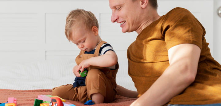 Father and son sitting on a bed playing with coloured blocks and toy cards.