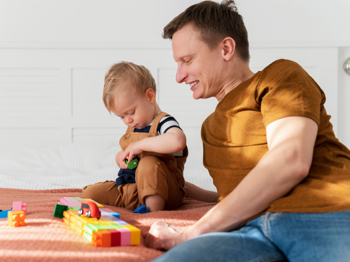 Father and son sitting on a bed playing with coloured blocks and toy cards.