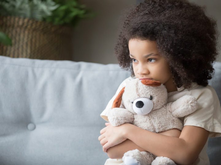 Young girl sitting on sofa hugging a teddy bear looking sad