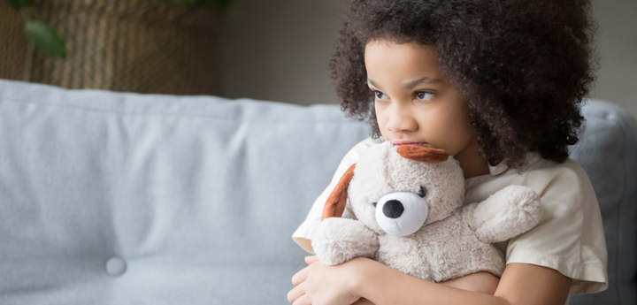 Young girl sitting on sofa hugging a teddy bear looking sad