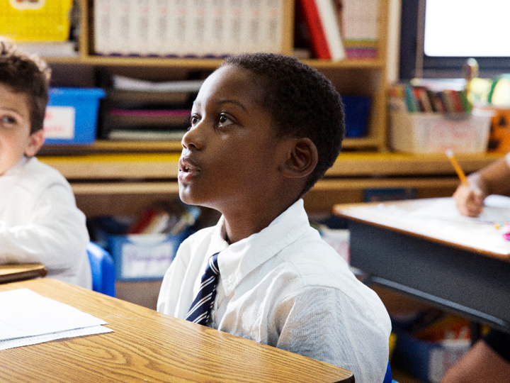 10 year old boy sitting in classroom at desk, looking up