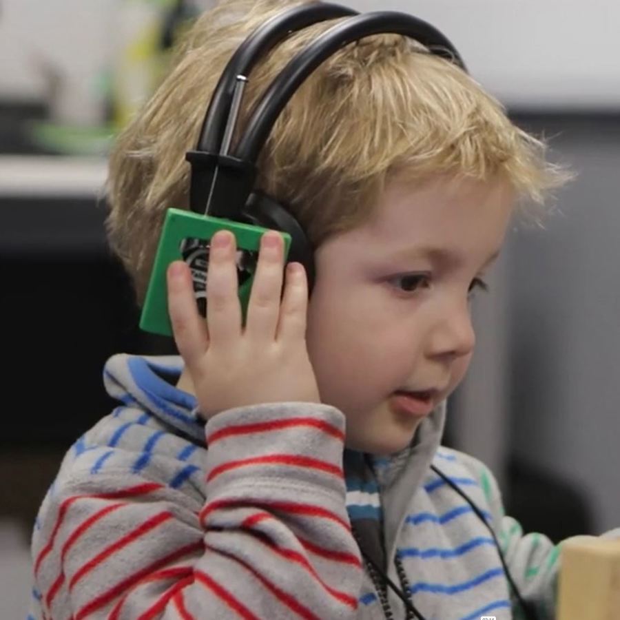 Young boy with headphones on holding a wooden block having a hearing test