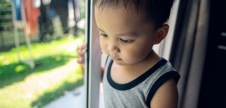 Young child standing and holding sliding glass door and looking down to the ground with garden in background