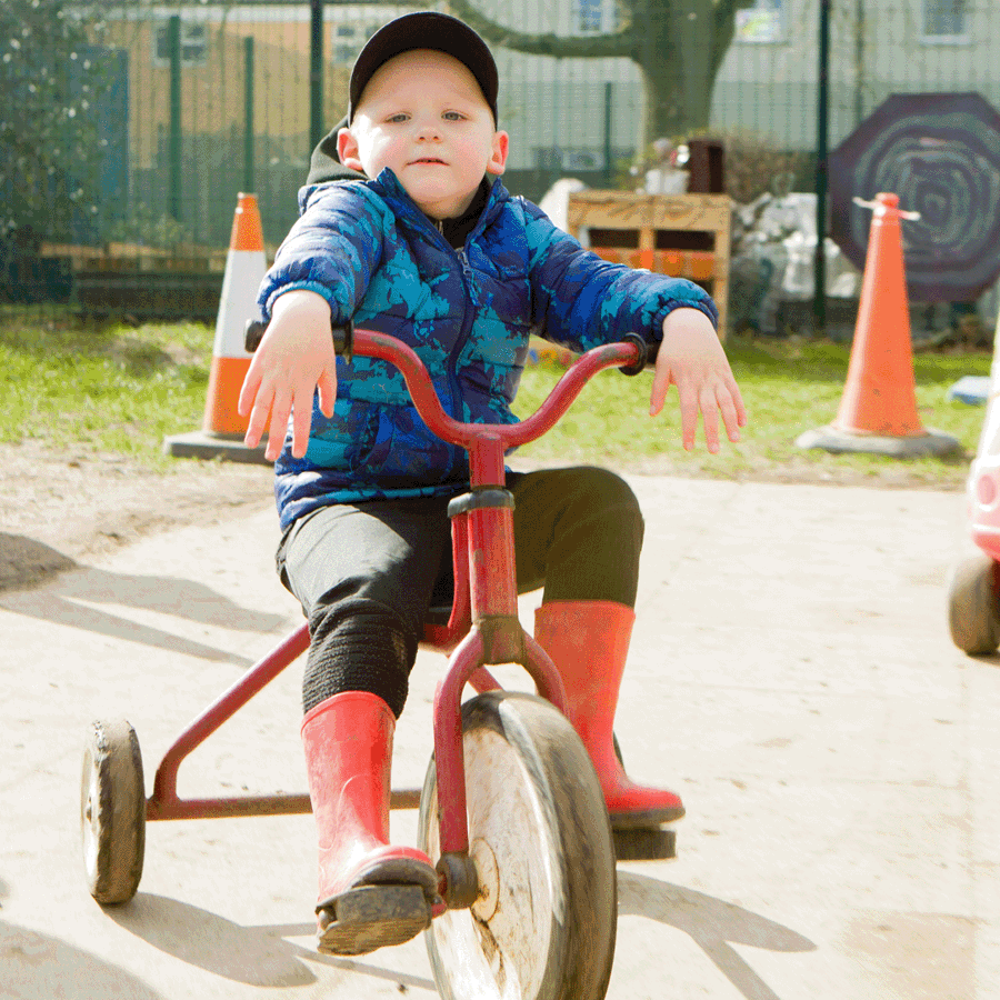 Boy sitting on tricycle with red and yellow car in background