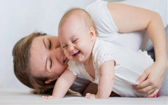 Baby in crawling position with adult smiling and holding the baby's hips