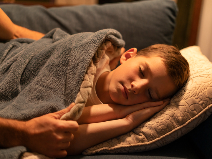 Image of a young boy sleeping while an adult tucks them into bed