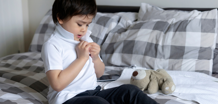 Young boy sitting on a bed buttoning up his white polo-shirt. 