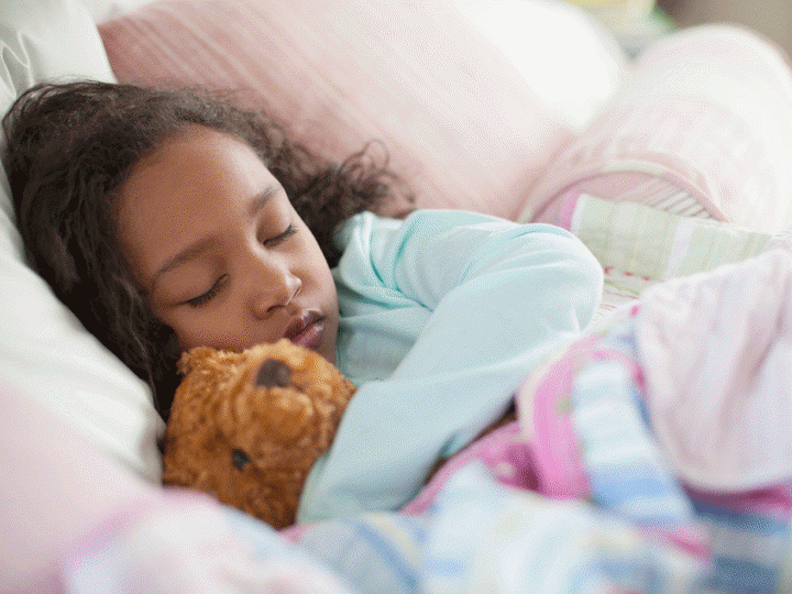 Young girl asleep in bed cuddling a teddy bear