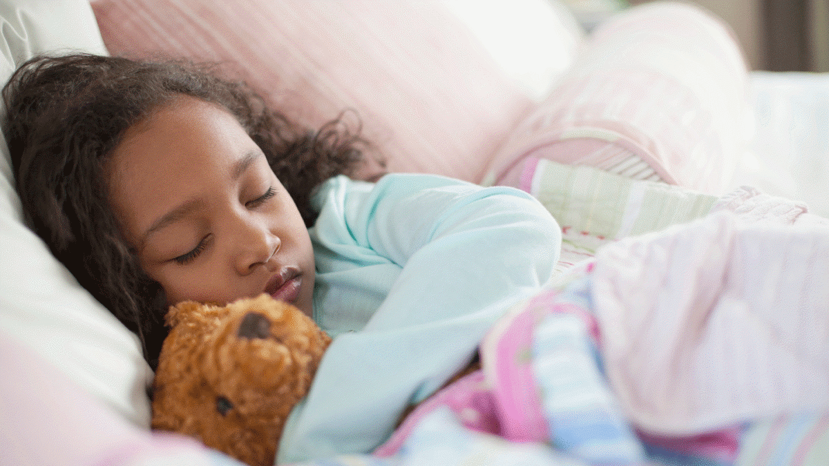 Young girl asleep in bed cuddling a teddy bear