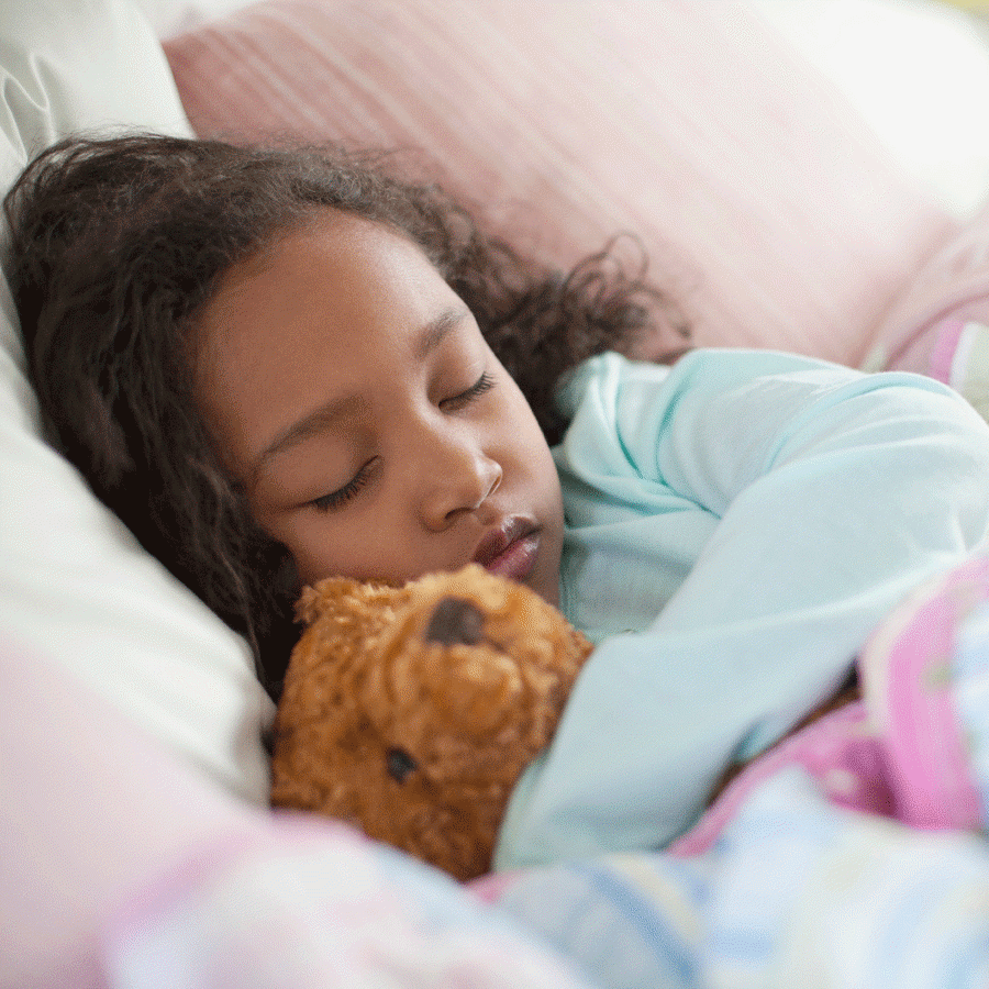 Young girl asleep in bed cuddling a teddy bear