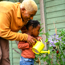 Smiling adult man helping a little girl to water some flowers in a garden with a bright yellow watering can.
